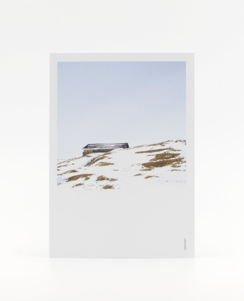 Postkarte im Polaroid Stil mit Alphütte auf Berghügel und blauem Himmel